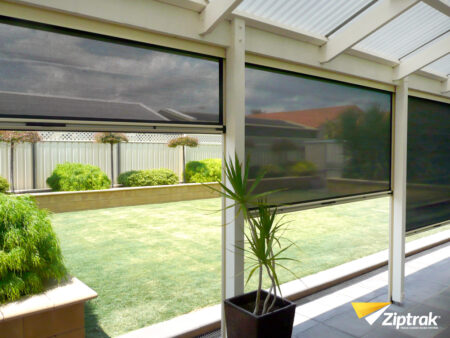 3 black zip trak blinds showing the stages of it being fully down on veranda .