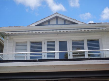 Front of home top balcony with Grey and white striped awning rolled up under eaves.