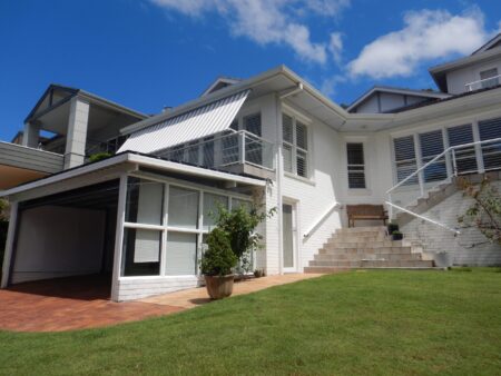 Side view of front of house with grey and white striped Voss Robb Pivot Awning extended to protect the house from sun.