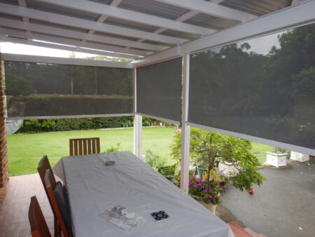 View from inside looking out at three vertical drop blinds half closed on backyard patio.