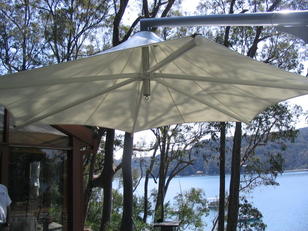 Open white Skyspan Umbrella next to house with view of water through trees.